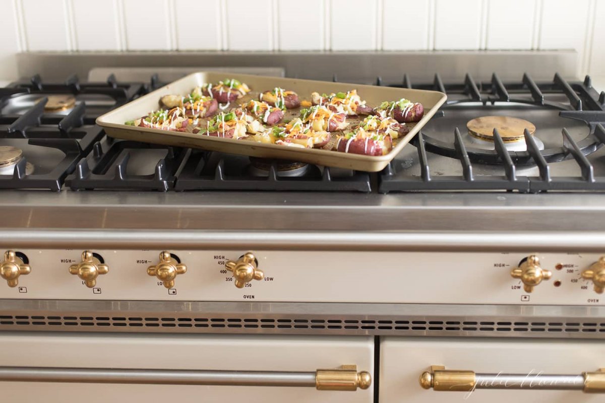Loaded smashed red potatoes on a gold baking sheet.