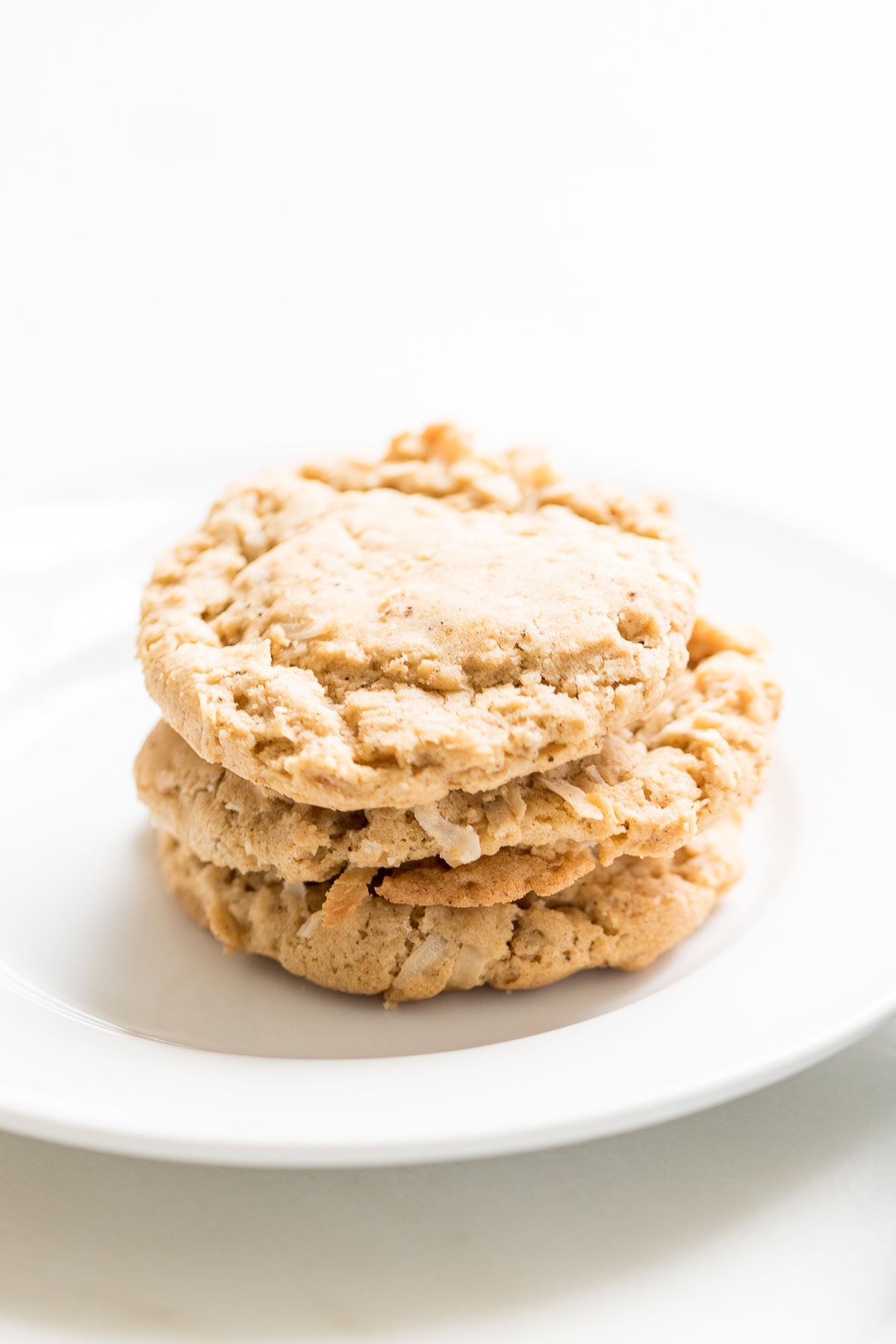 A stack of three delicious oatmeal coconut cookies sits invitingly on a pristine white plate.