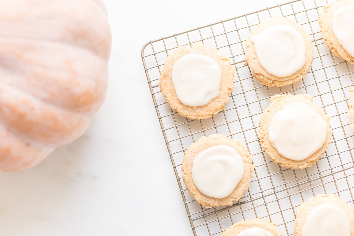 pumpkin sugar cookies with cream cheese glaze on a cooling rack