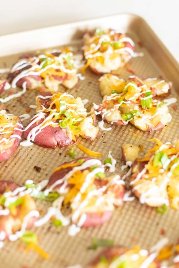 Loaded smashed red potatoes on a gold baking sheet.