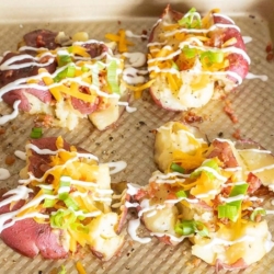 Loaded smashed red potatoes on a gold baking sheet.
