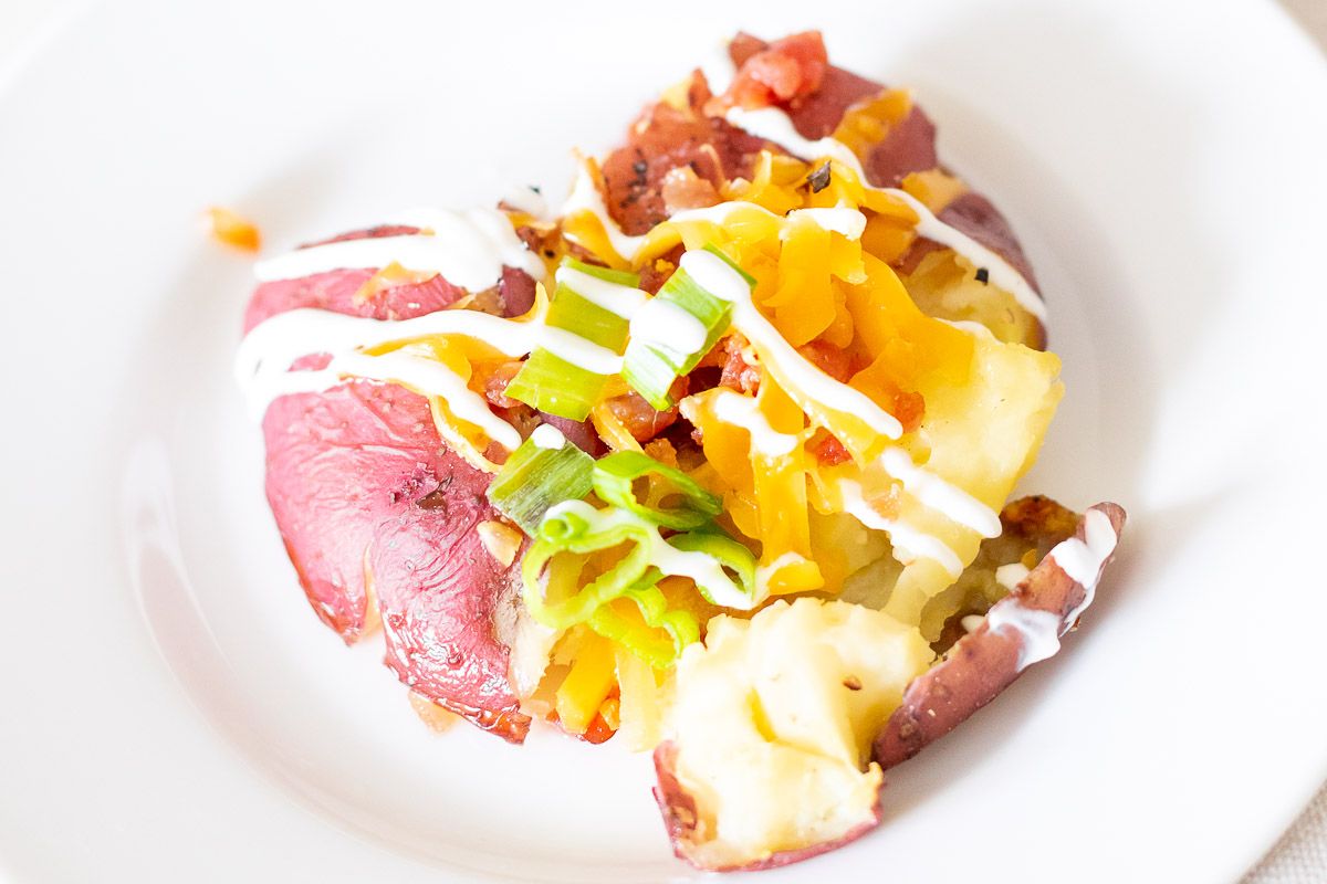 A loaded smashed red potato on a white plate.