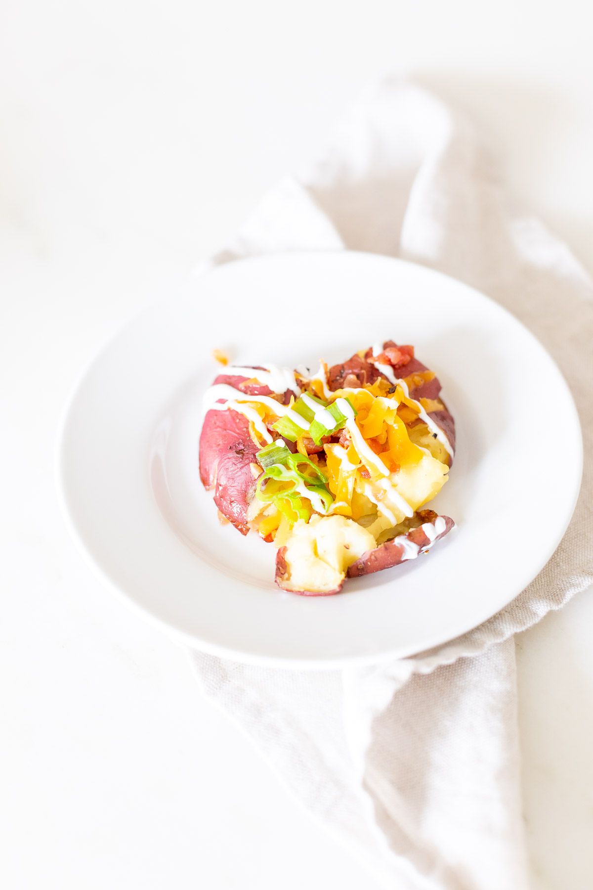 A loaded smashed red potato on a white plate.