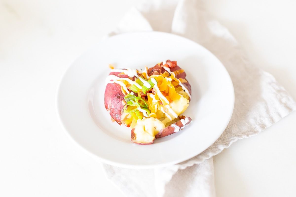 A loaded smashed red potato on a white plate.