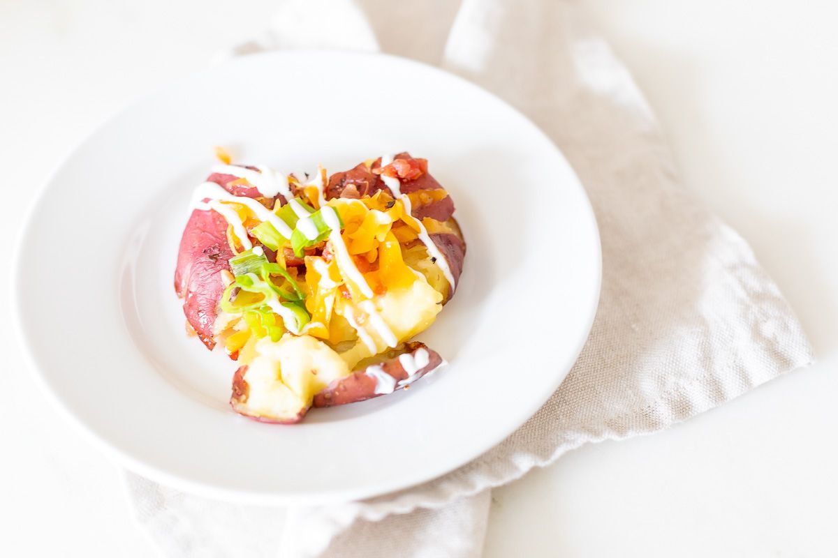 A loaded smashed red potato on a white plate.