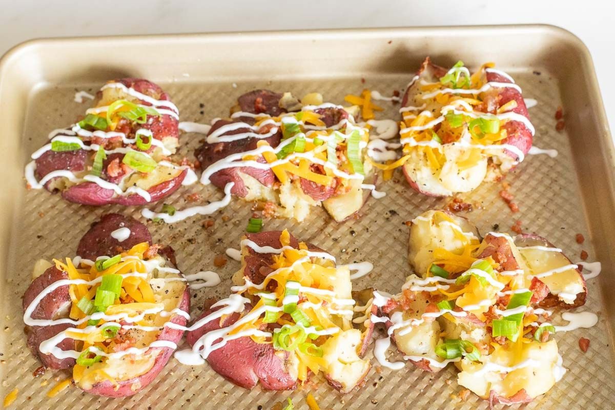 Loaded smashed red potatoes on a gold baking sheet.