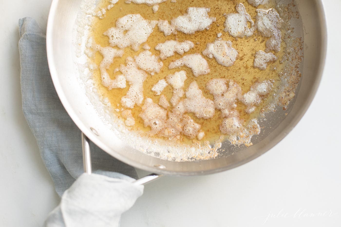 A silver pan with handle, warm browned butter inside, showing how to brown butter.