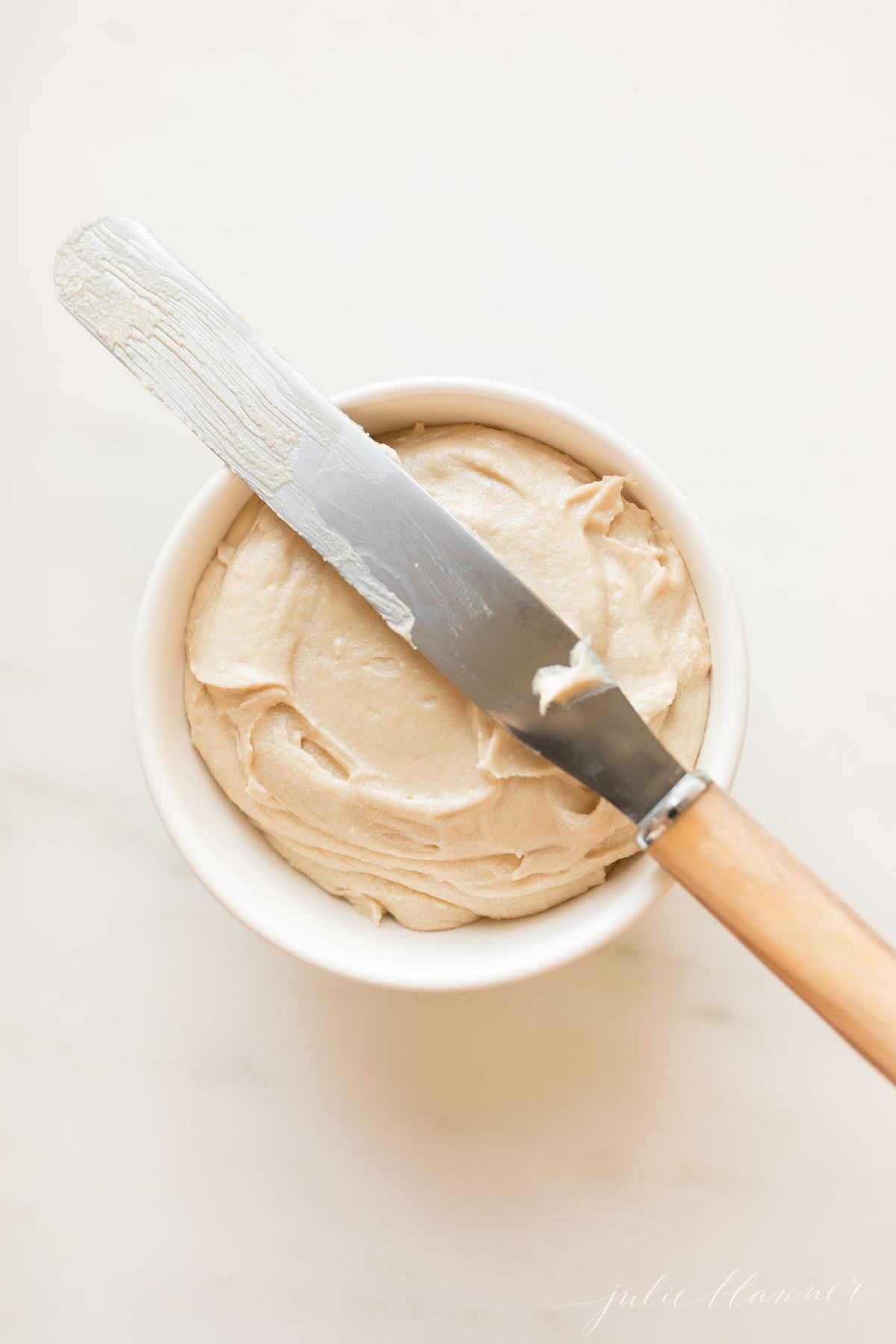 Caramel icing in a small white bowl with a pallet knife