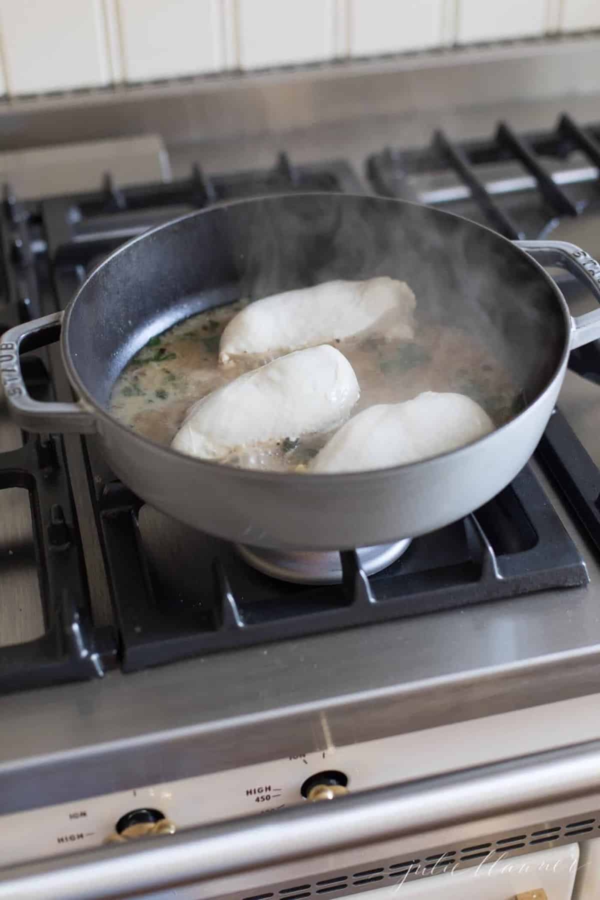 Chicken breasts in a gray cast iron saute pan on the stove.