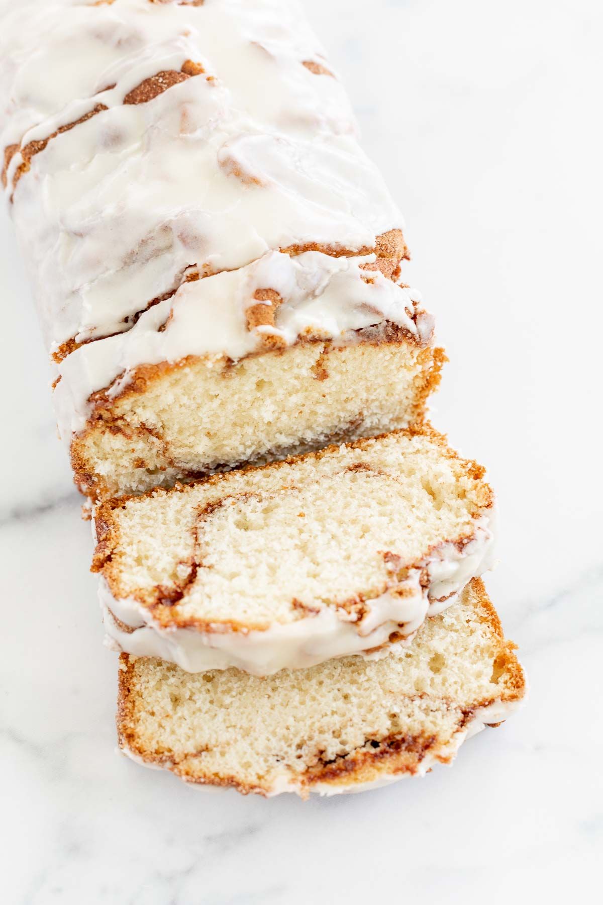 A loaf of cinnamon roll bread, covered in icing and sliced on a marble surface