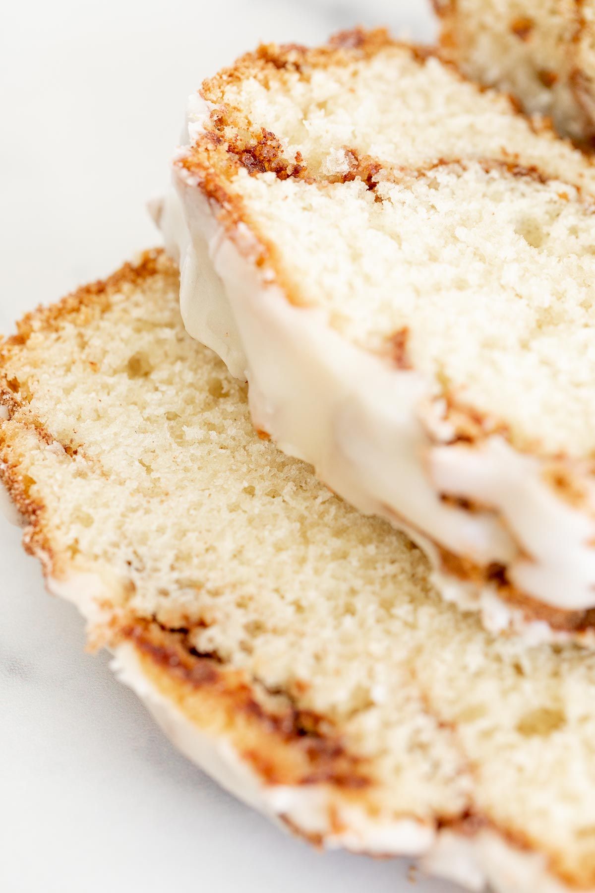 A loaf of cinnamon roll bread, covered in icing and sliced on a marble surface