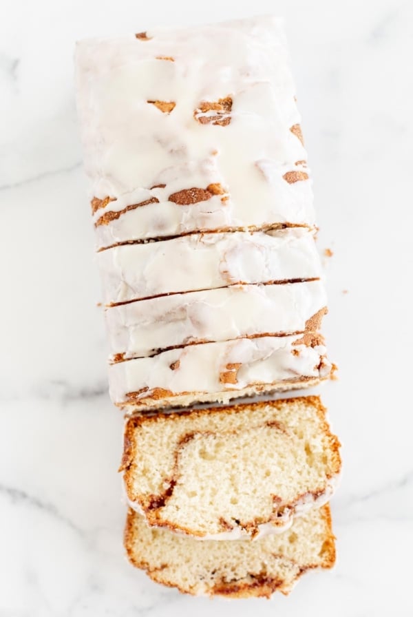 A loaf of cinnamon roll bread, covered in icing and sliced on a marble surface