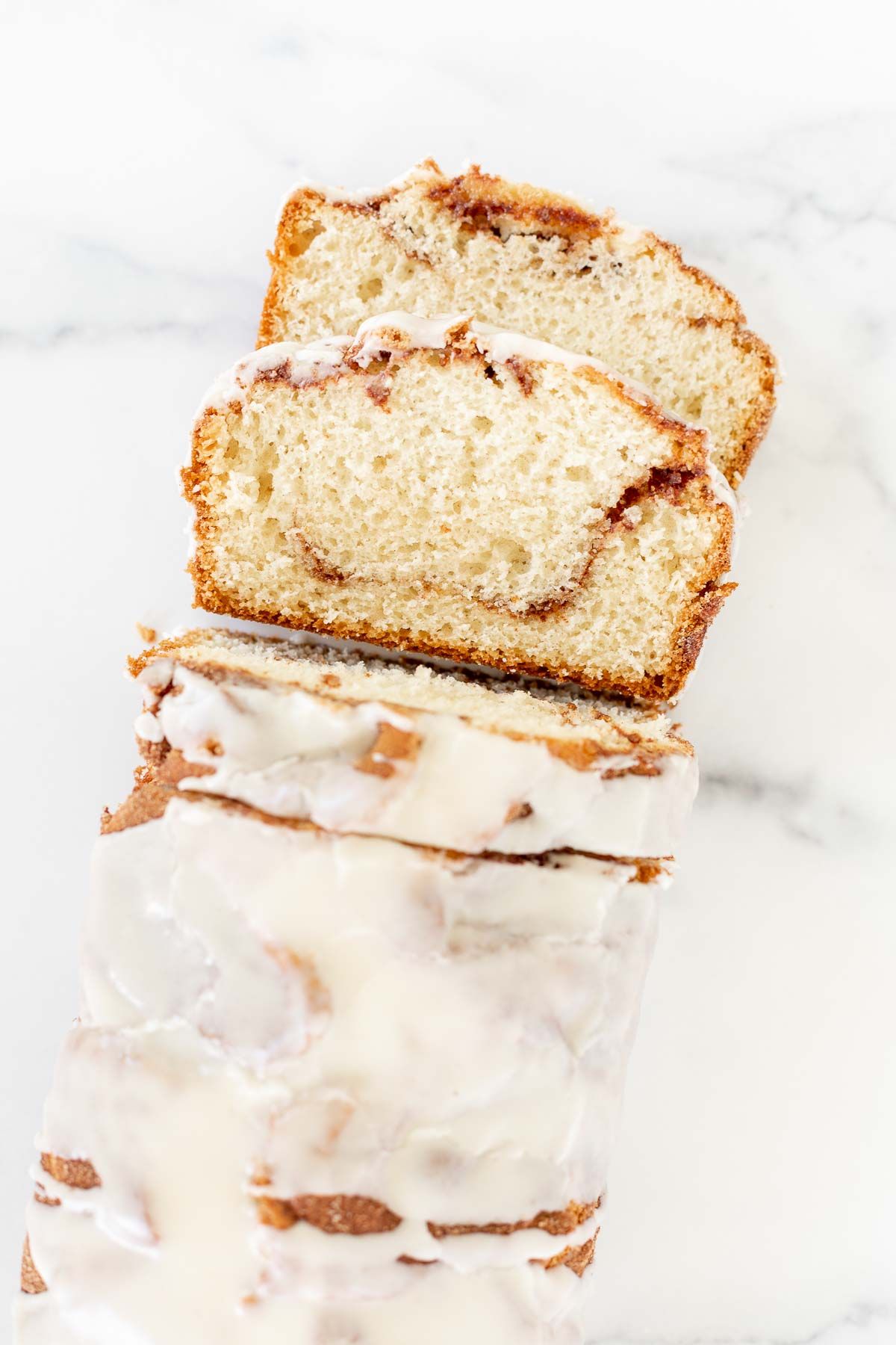 A loaf of cinnamon roll bread, covered in icing and sliced on a marble surface