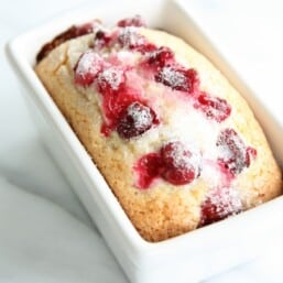 A small loaf of a cranberry bread recipe in a white ceramic loaf pan, white background.