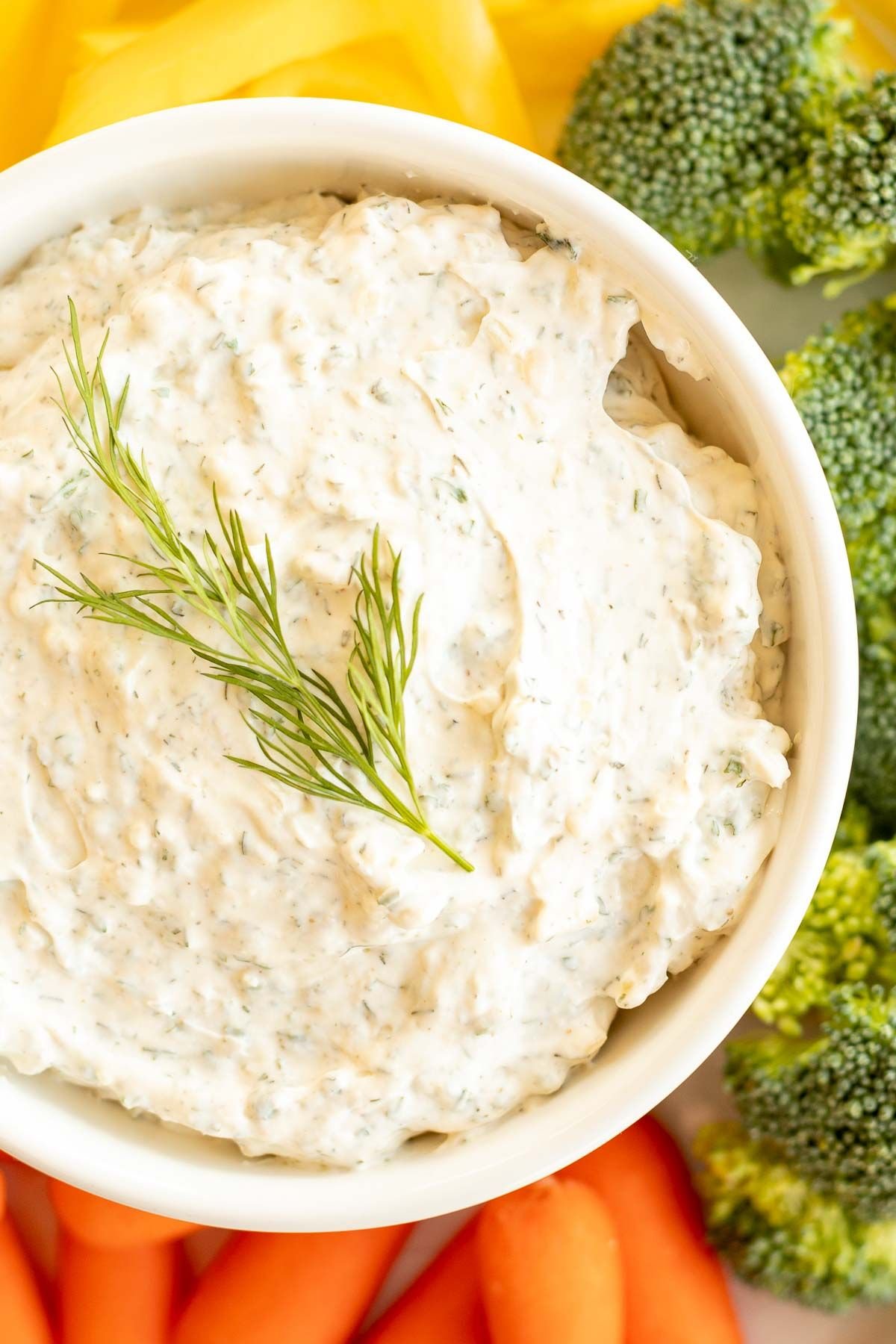 A hand dipping a chunk of bread into a bowl of a dill dip recipe.