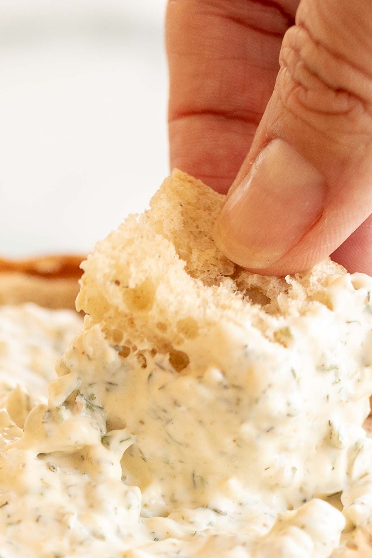 A hand dipping a chunk of bread into a bowl of a dill dip recipe.