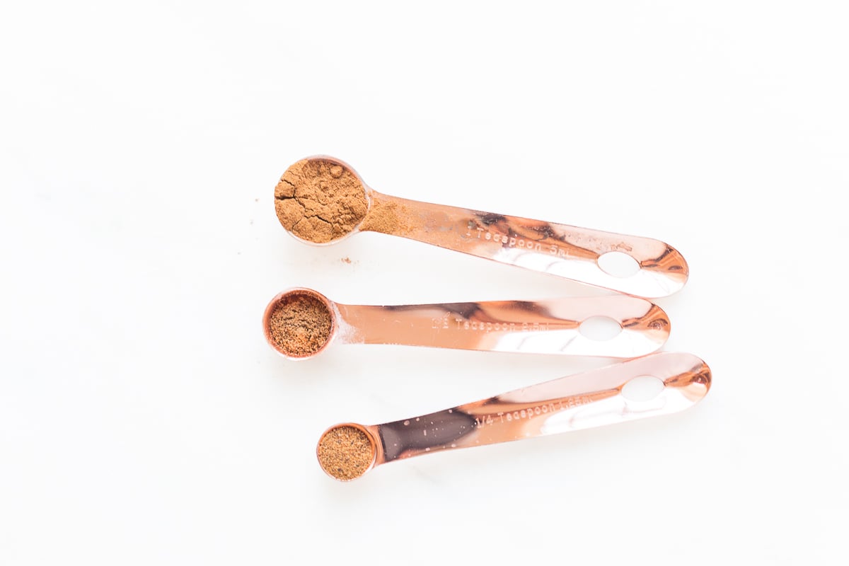 3 copper measuring spoons filled with spices on a white countertop.