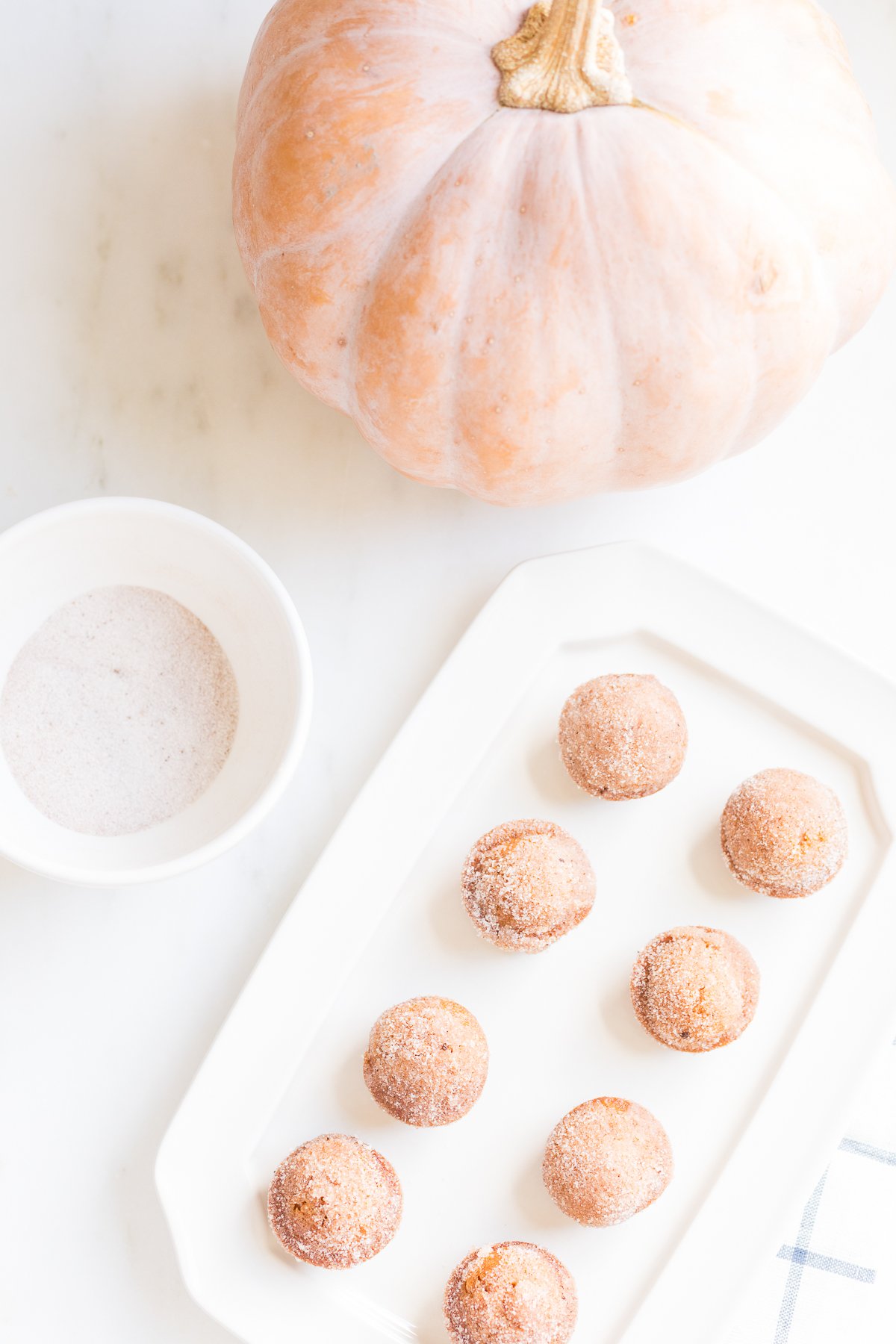 A platter of mini pumpkin muffins with a bowl of sugar and a peach pumpkin in the background.