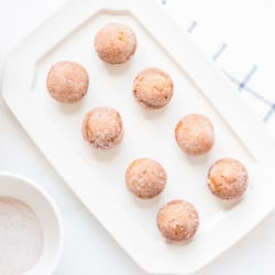 A platter of mini pumpkin muffins with a bowl of sugar and a peach pumpkin in the background.