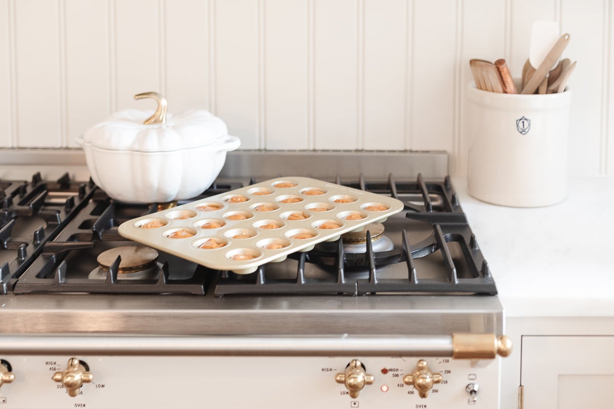 A gold mini muffin pan full of a mini pumpkin muffin recipe, on a stovetop.