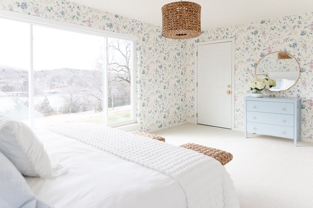 A bedroom with floral wallpaper and wall to wall carpeting.