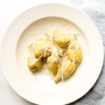 baked artichoke garnished with parmesan in cream serving bowl