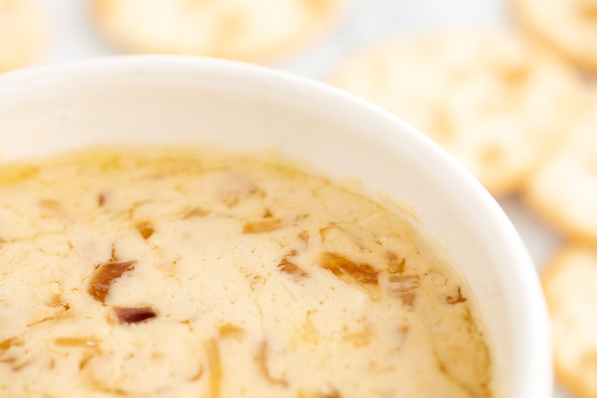 A white bowl of caramelized shallot dip, crackers in the background