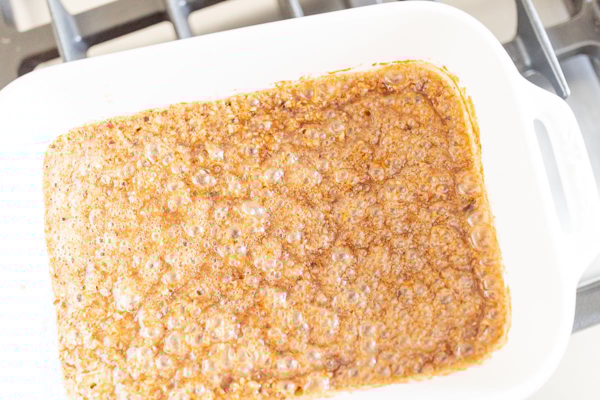 A square baking dish with caramel sauce inside it for pecan sticky rolls.