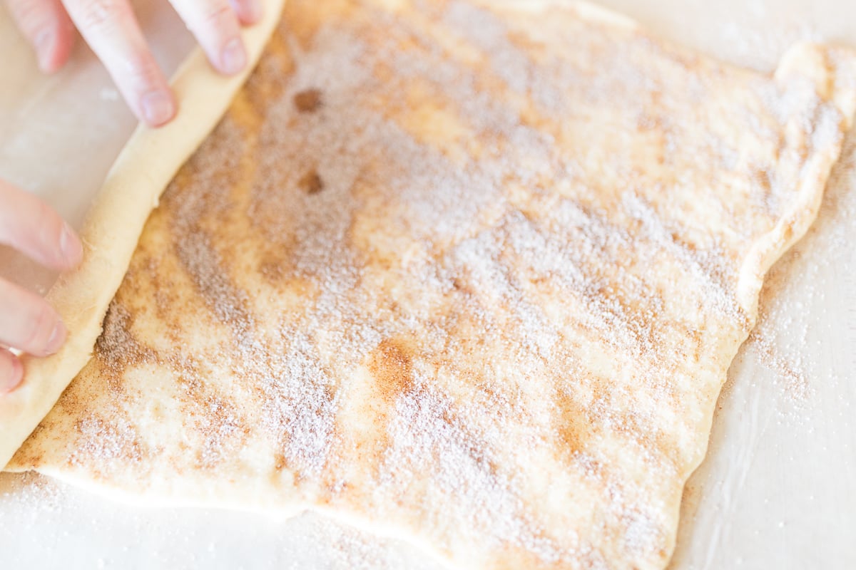 A person preparing pecan rolls with cinnamon sugar on a piece of dough.