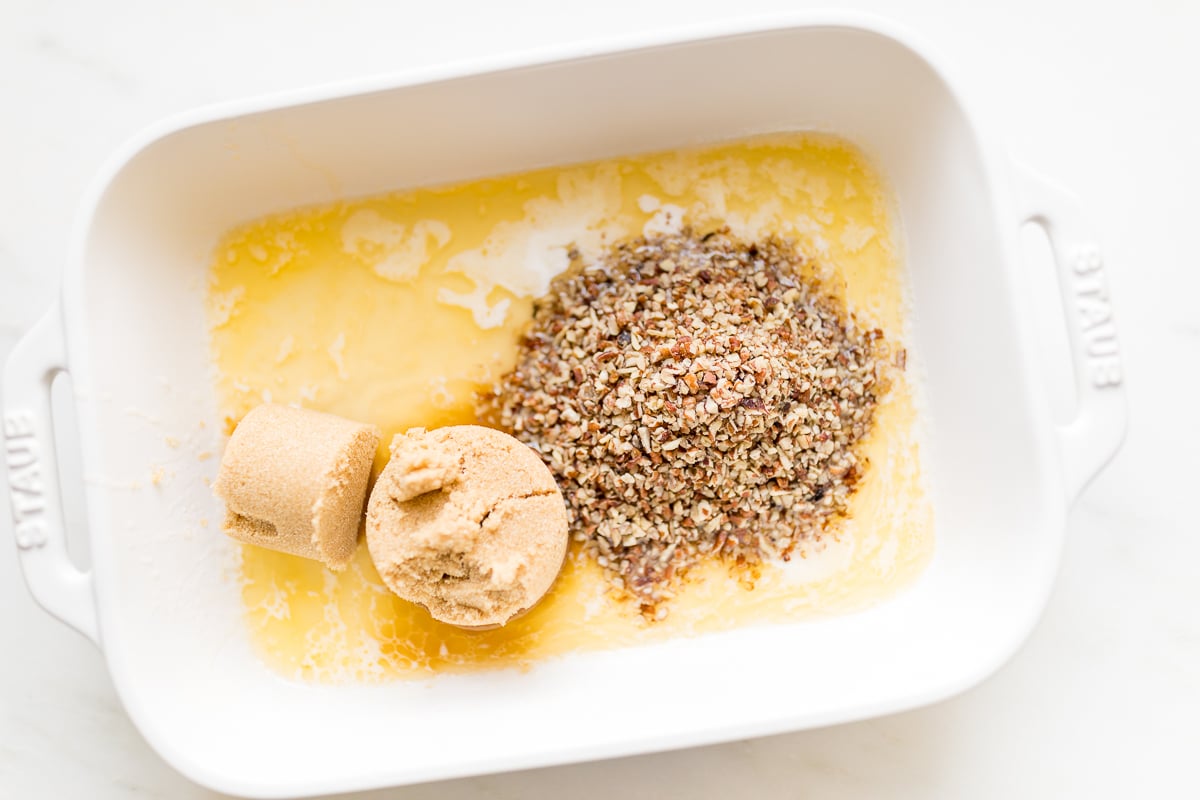 Brown sugar and pecans and butter in a white baking dish.