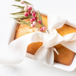 Almond bread in a white loaf pan tied with a white satin bow and a touch of pink berries.