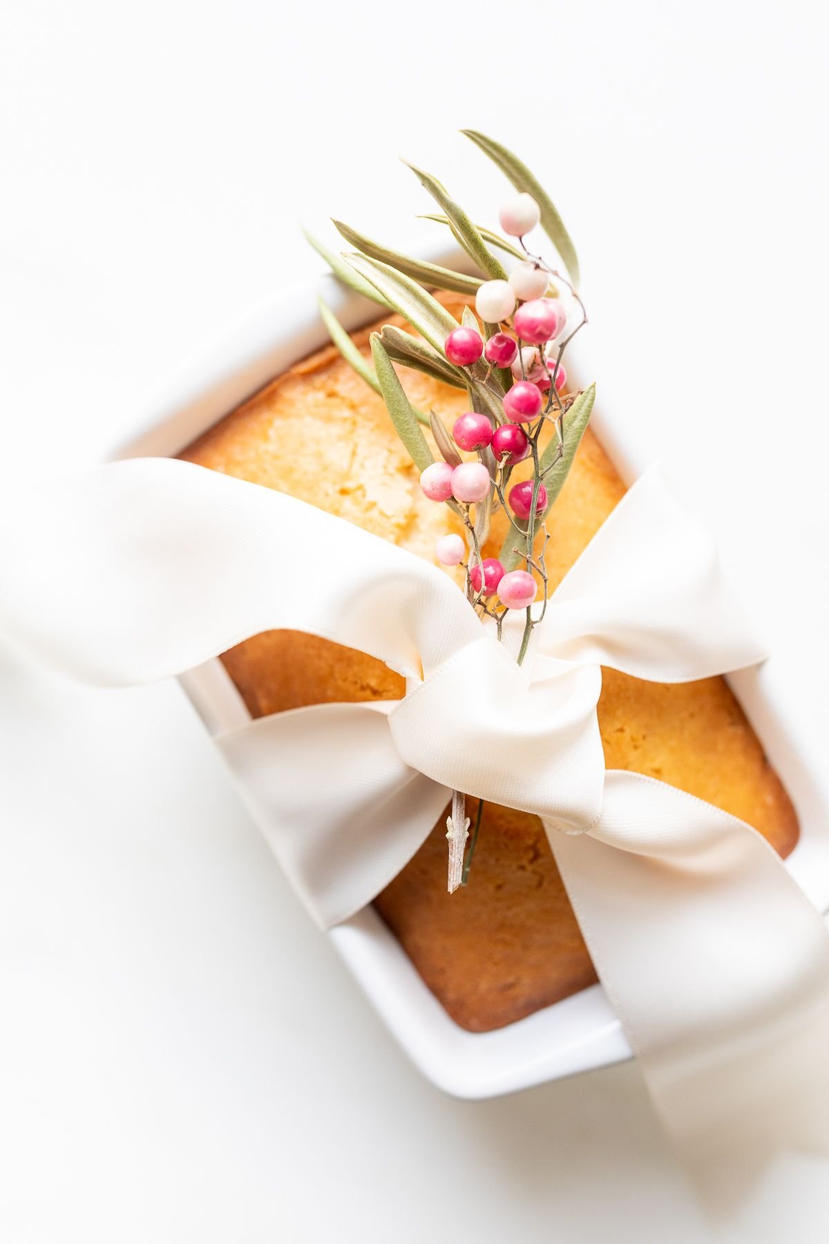 Almond bread in a white loaf pan tied with a white satin bow and a touch of pink berries.