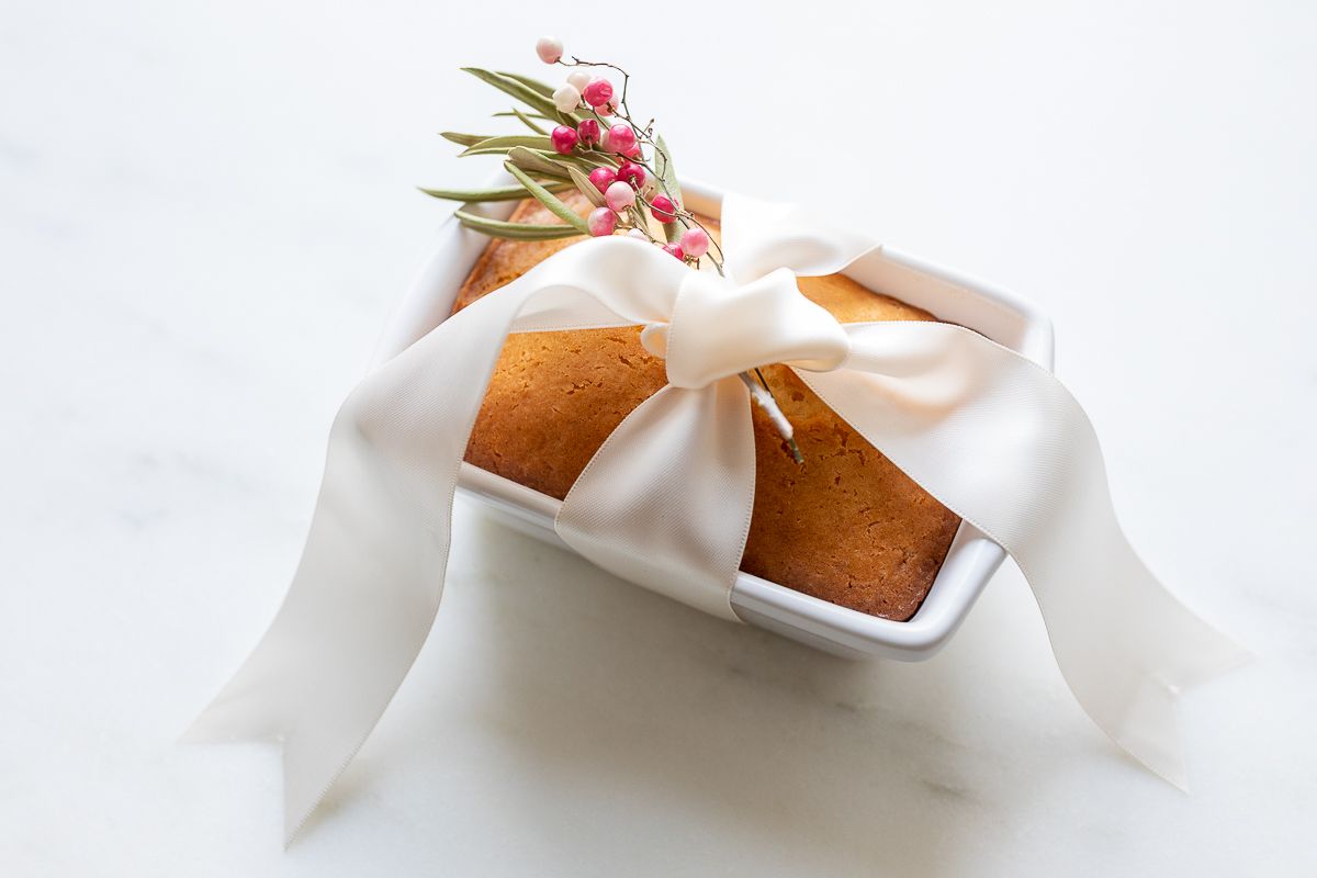 Almond bread in a white loaf pan tied with a white satin bow and a touch of pink berries.