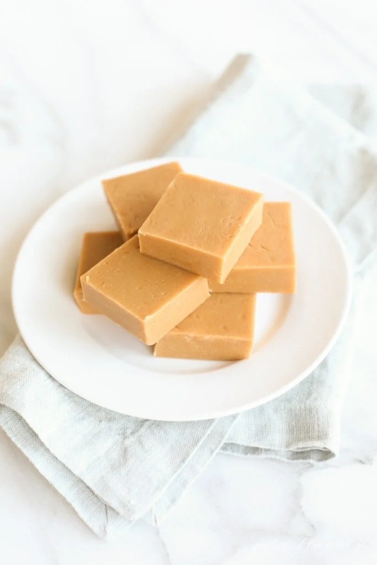 A stack of peanut butter fudge on a white plate, sitting atop a blue linen towel. .