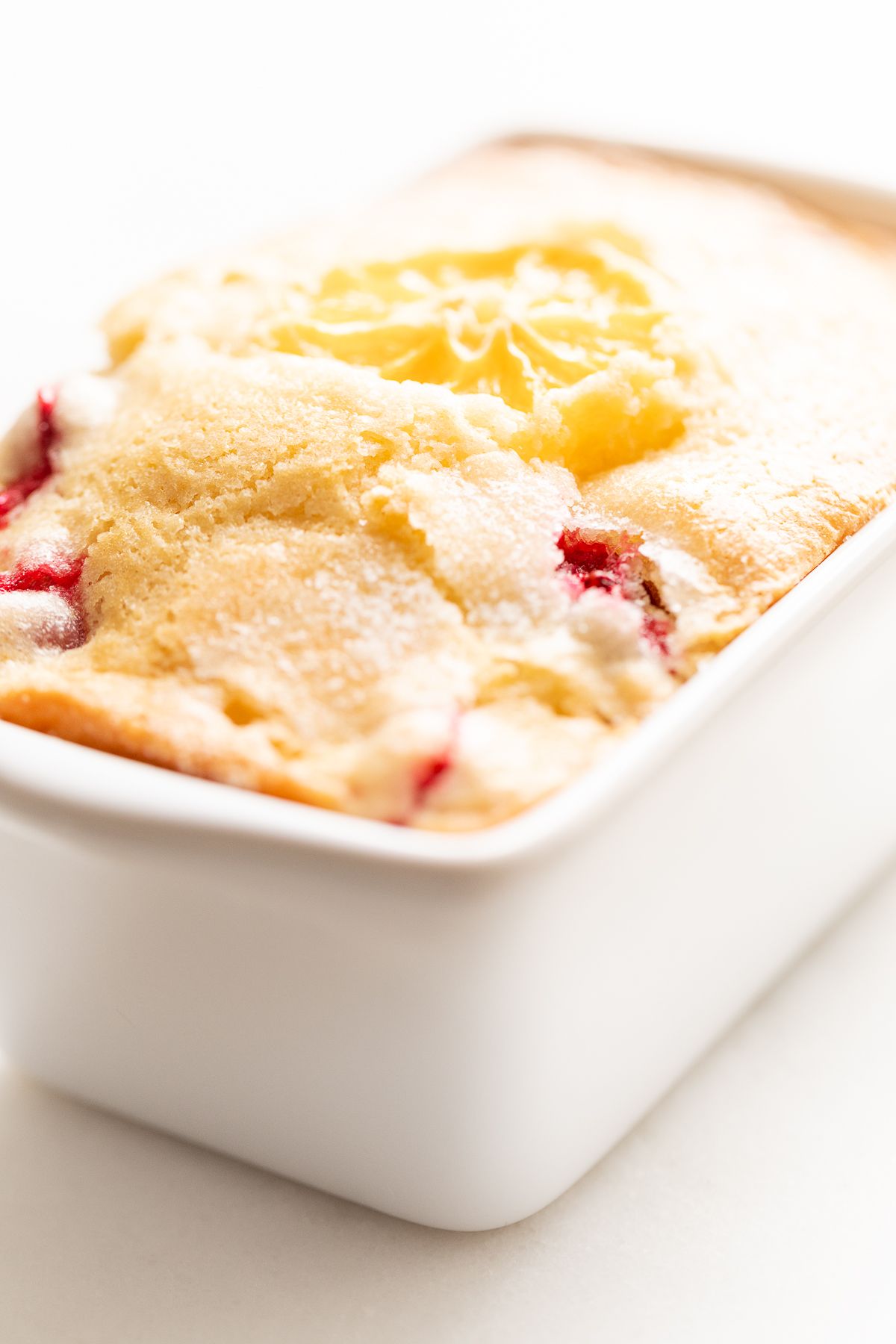 A small ceramic loaf pan filled with fresh cranberry orange bread.
