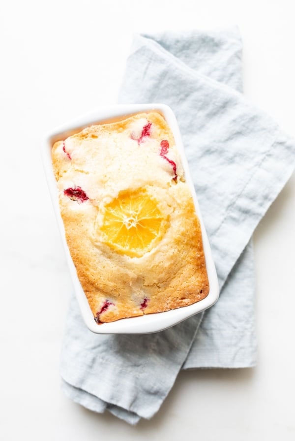 Small ceramic loaf pan of cranberry orange bread, resting on a pale blue linen towel.