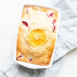 Small ceramic loaf pan of cranberry orange bread, resting on a pale blue linen towel.