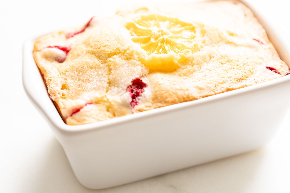 A small ceramic loaf pan filled with fresh cranberry orange bread.