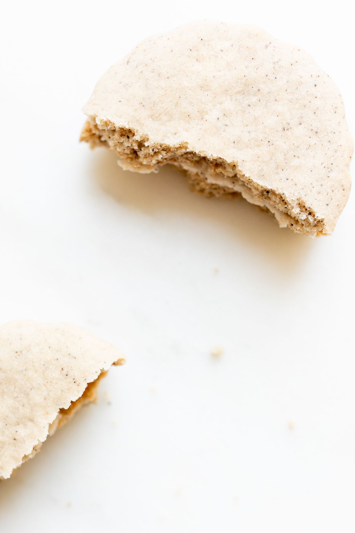 Latte cookie with filling between two layers, broken in half on a white countertop.