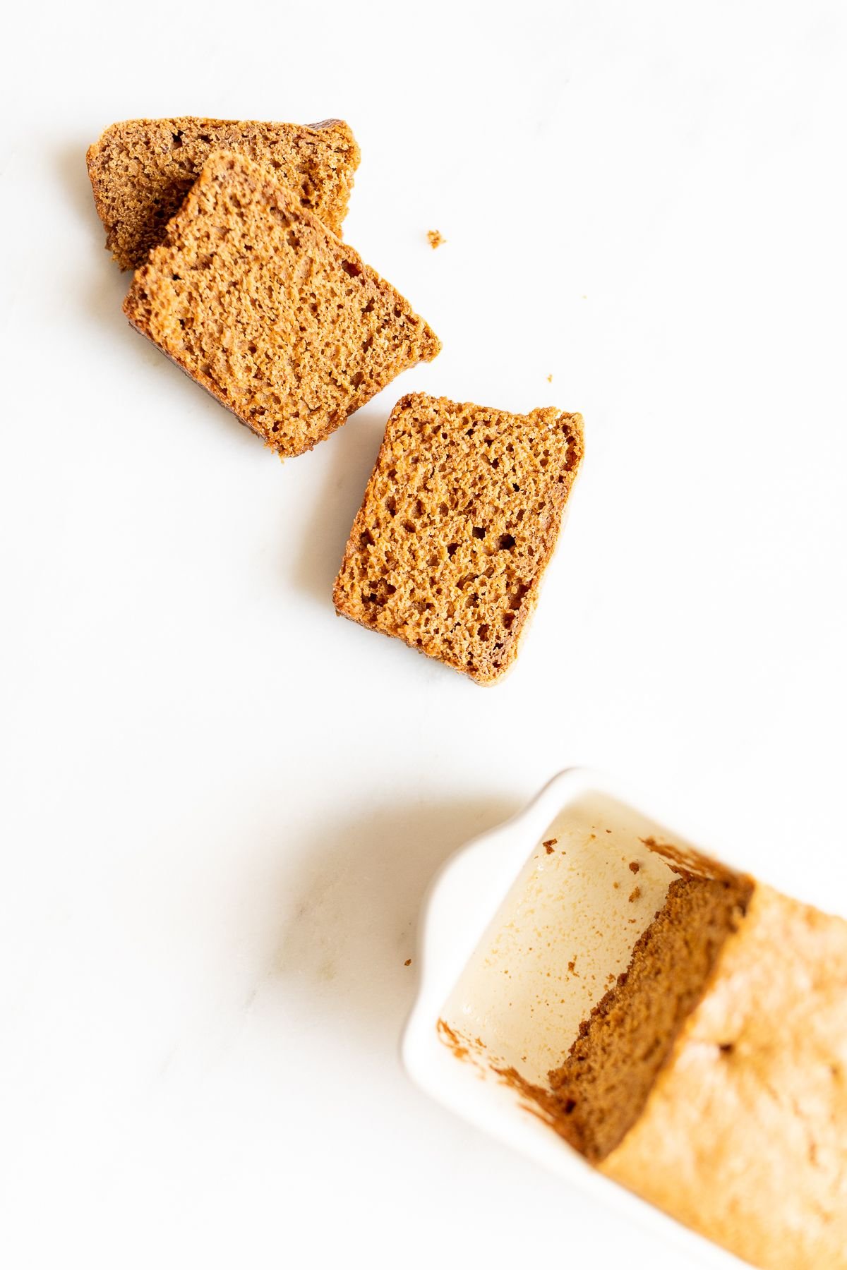 Slices of gingerbread loaf next to a loaf in a white loaf pan.