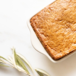 A gingerbread loaf in a white ceramic loaf pan, with an olive branch beside it.