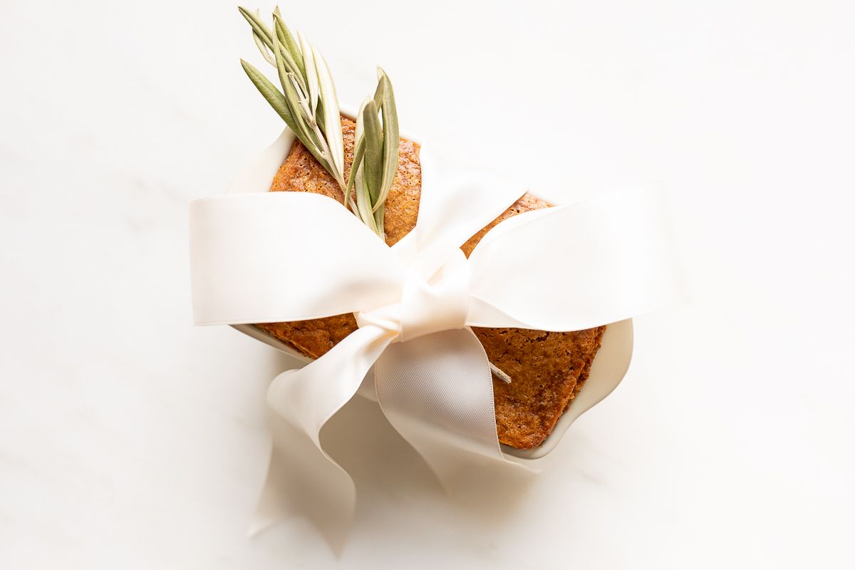 A gingerbread loaf in a white ceramic loaf pan, with an olive branch beside it.