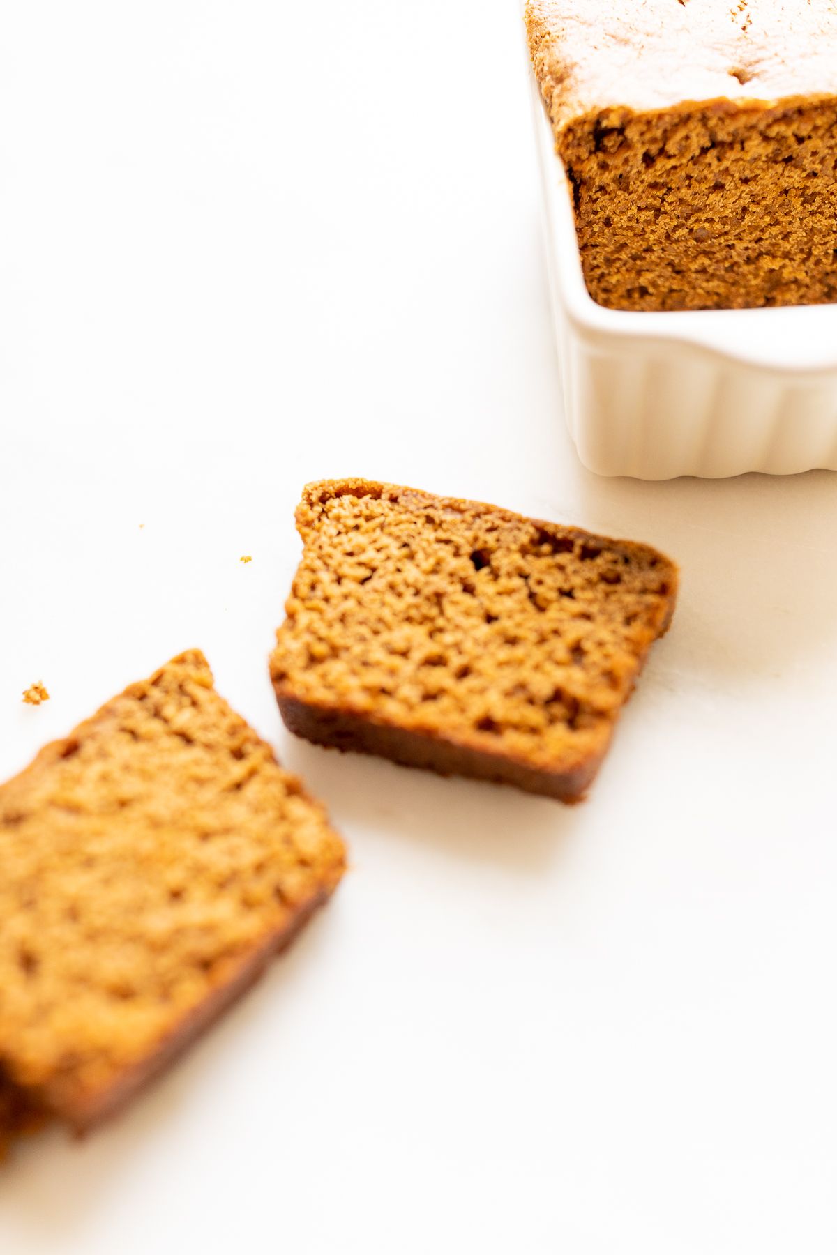 Slices of gingerbread loaf next to a loaf in a white loaf pan.