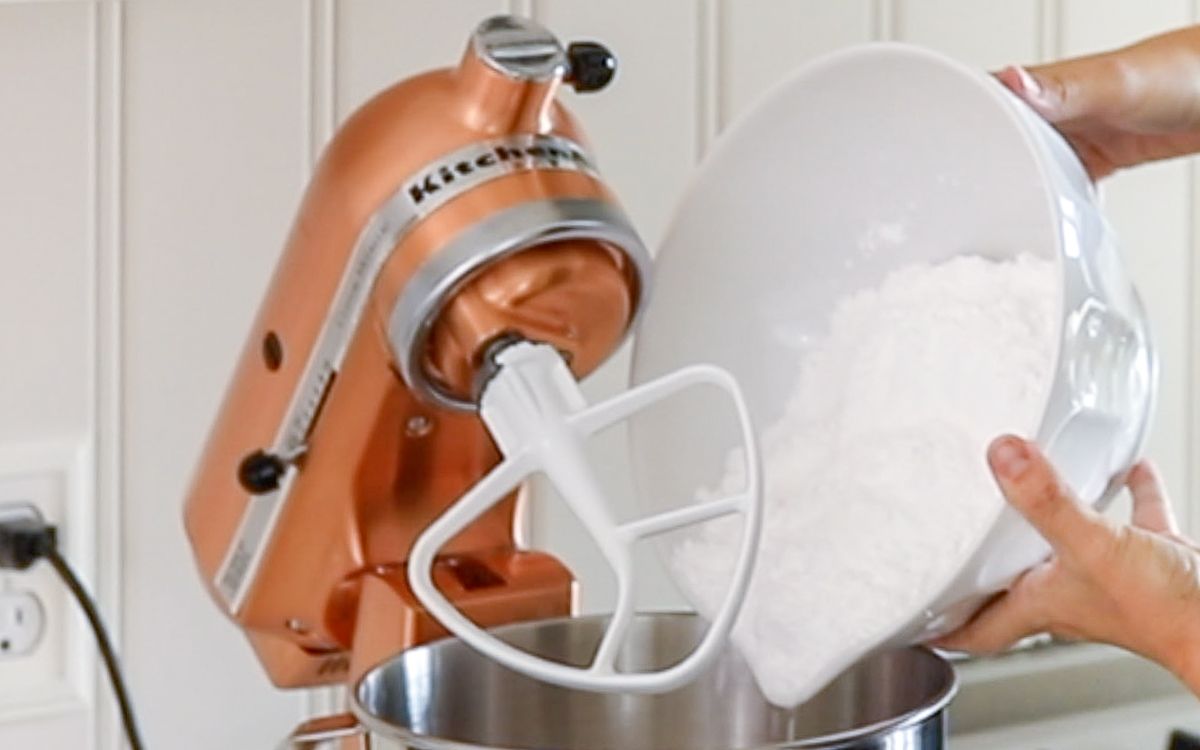 A copper stand mixer with ingredients for peanut butter fudge being added in by a pair of hands.