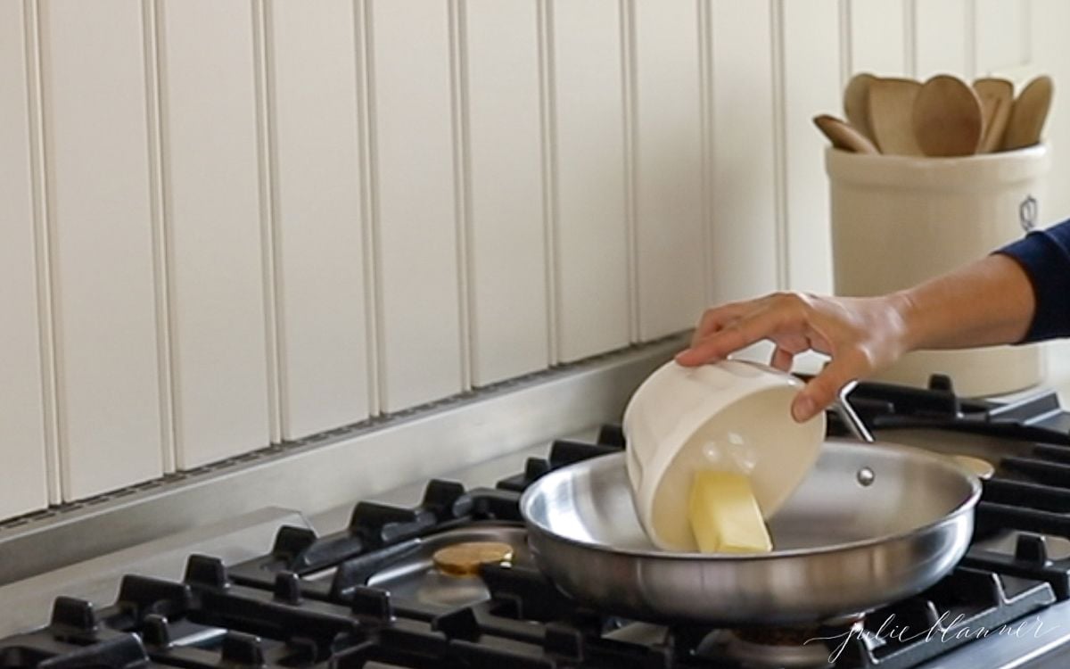 A silver pan on a stovetop with a hand mixing up peanut butter fudge