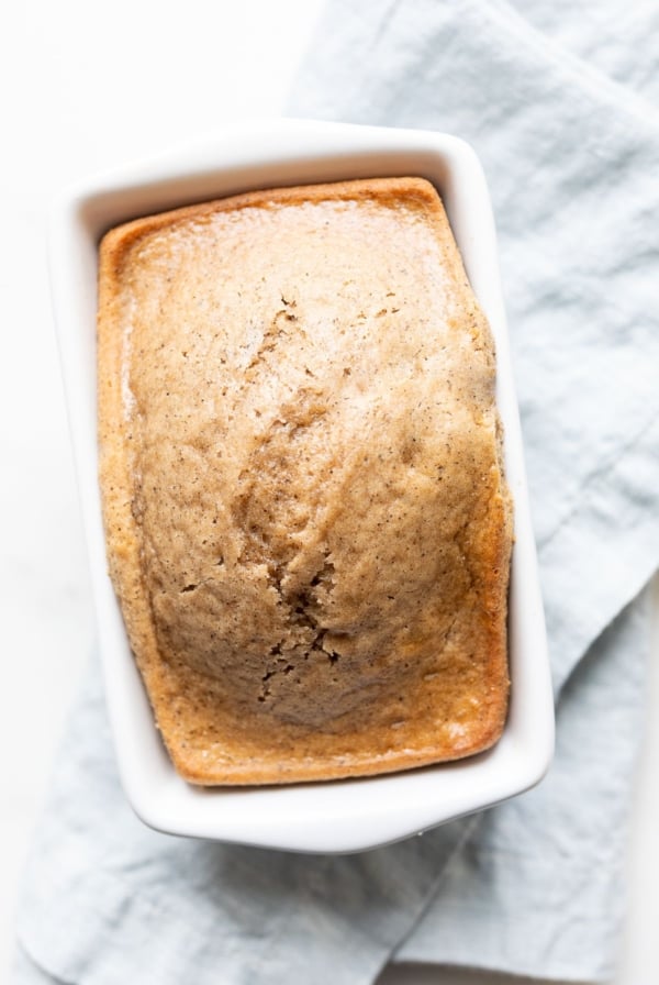 A quick latte bread in a small white loaf pan, on a blue kitchen towel.