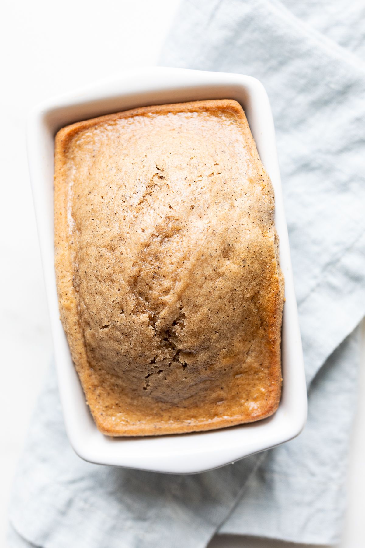 A quick latte bread in a small white loaf pan, on a blue kitchen towel.