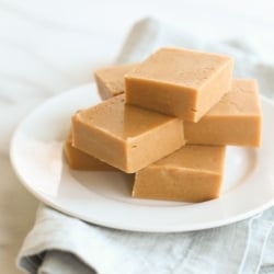 A stack of peanut butter fudge on a white plate, sitting atop a blue linen towel. .