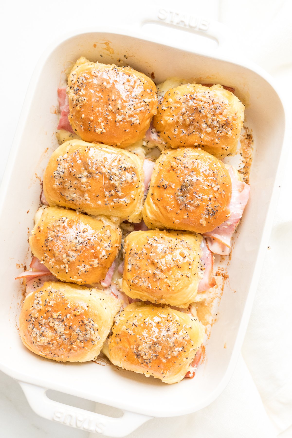 Hot ham and cheese sliders in a white baking dish.