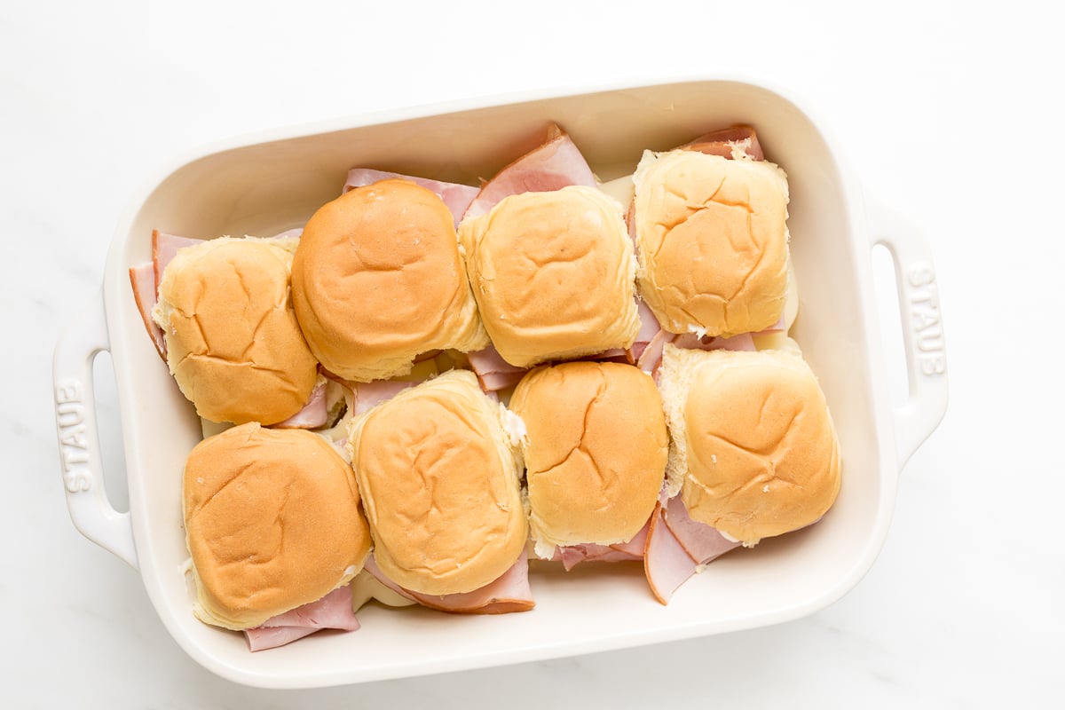 Hot ham and cheese sliders in a white baking dish.